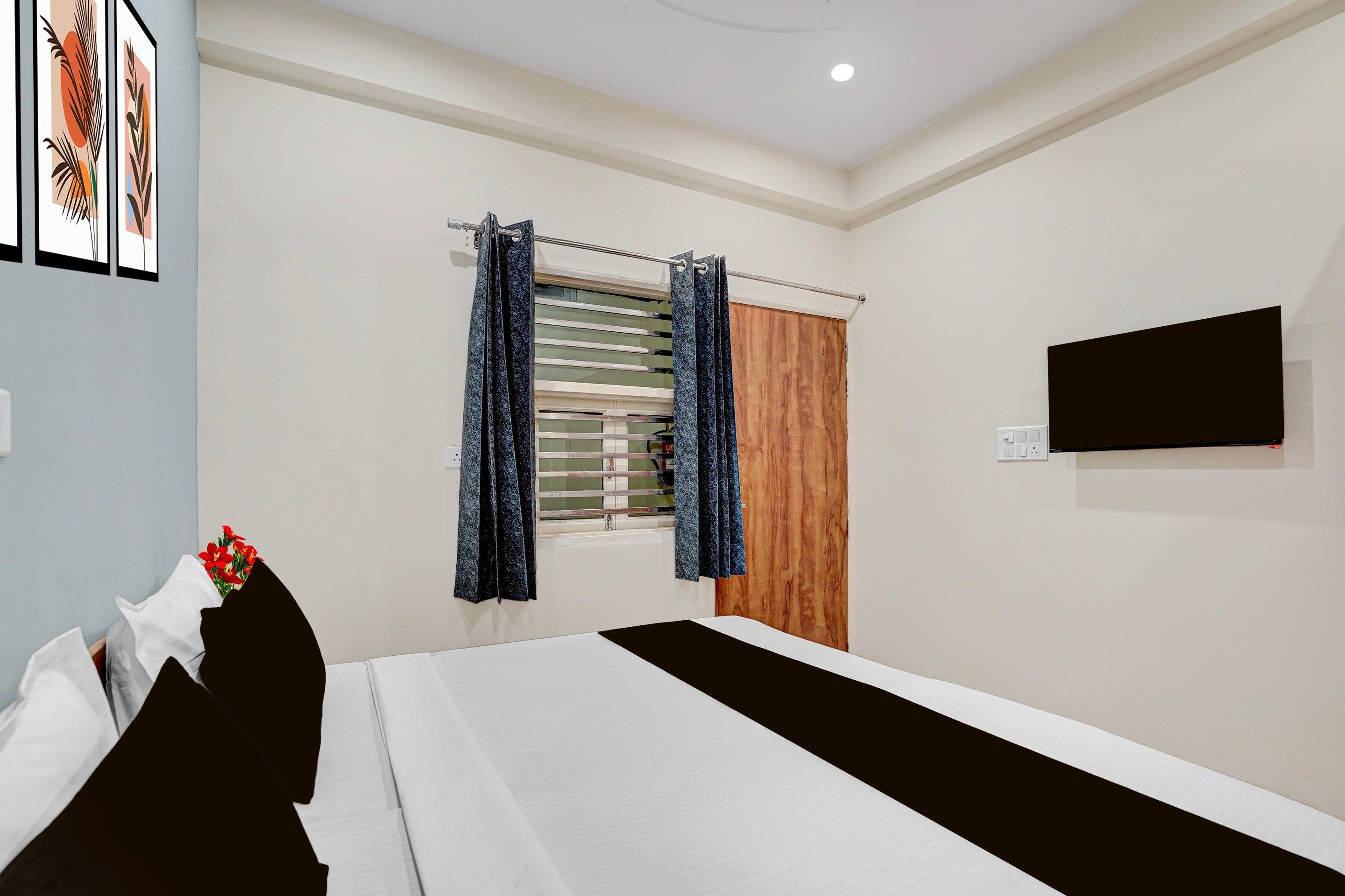 Een hotelkamer met een bed, een raam met gordijnen, een houten deur en een flatscreen televisie die aan de muur is bevestigd.