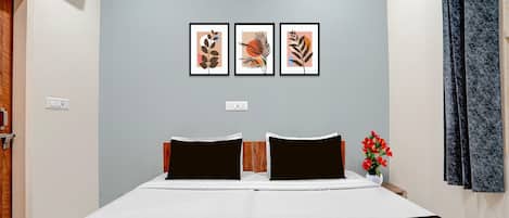 A bedroom with a bed, two pillows, a nightstand with a vase of flowers, and three framed artworks on the wall.