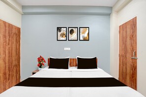 A hotel room with a bed, two bedside tables, a nightstand, a vase with flowers, and three framed artworks on the wall. - Ollection O Sector 95B Gurgaon (Gurugram)