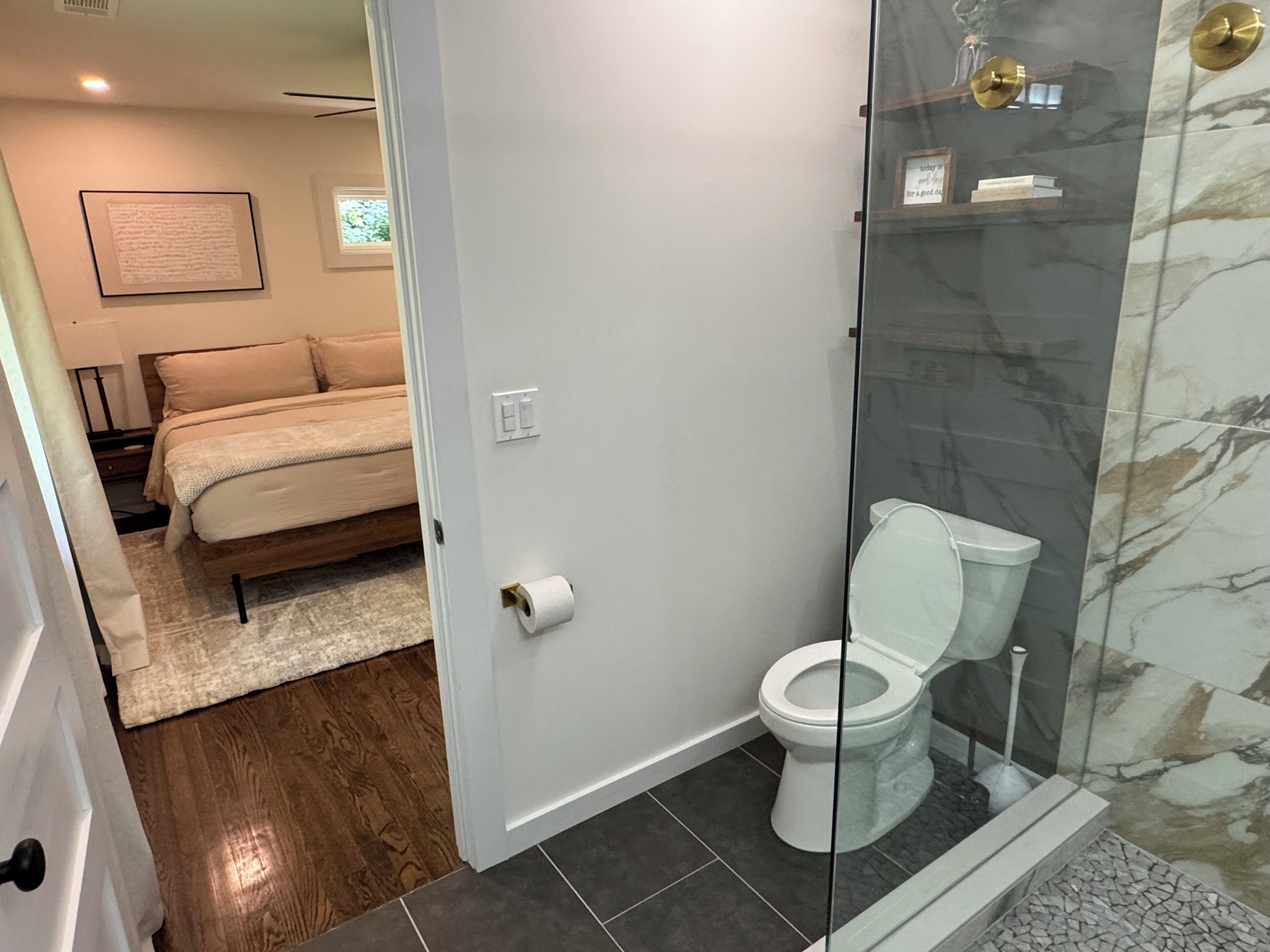 A modern bathroom with a glass shower enclosure, a toilet, and a visible roll of toilet paper.