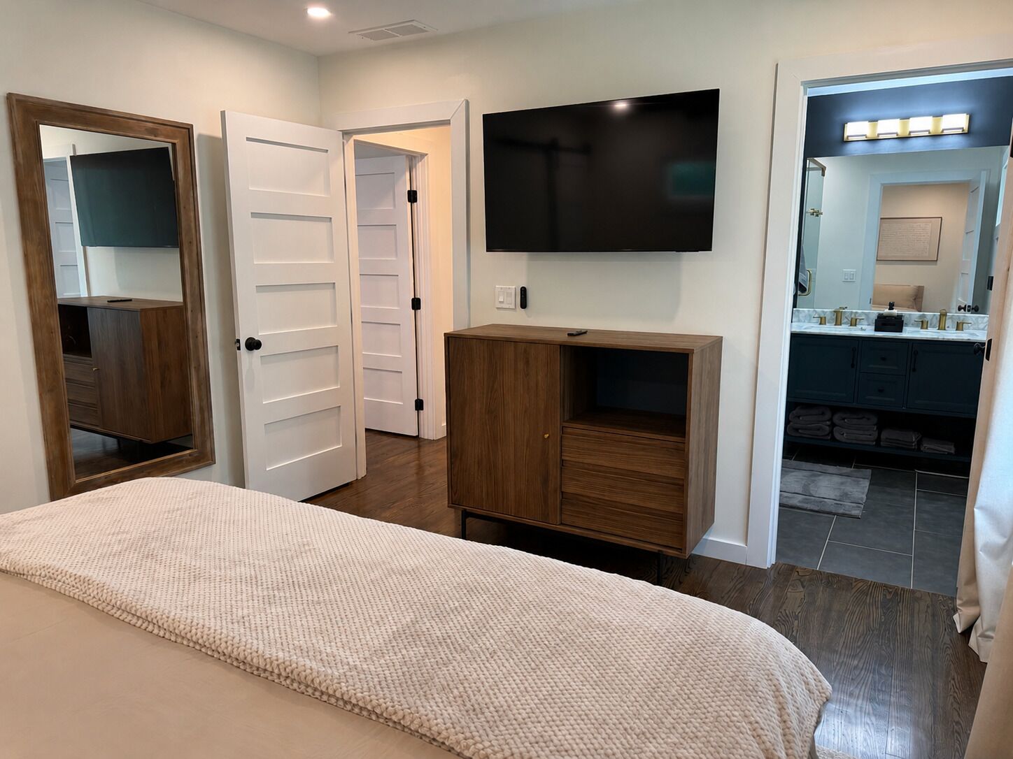 A bedroom with a bed, a TV mounted on the wall, a wooden cabinet, and a bathroom visible through an open door.