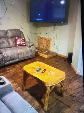 A living room with a leather sofa, a wooden coffee table with remotes, a television mounted on the wall, and a wooden cabinet. - Cabin 38 miles from Beach Mountain ski resort 5 miles from the lake in winery (Butler)