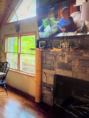 A room with a stone fireplace, a window with a view of greenery, and a chair. - Cabin 38 miles from Beach Mountain ski resort 5 miles from the lake in winery (Butler)