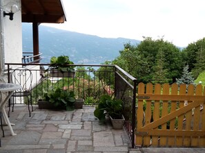 A balcony with stone flooring, potted plants, a table, and a view of mountains. - Casa Giuseppe by Interhome (Manerba)