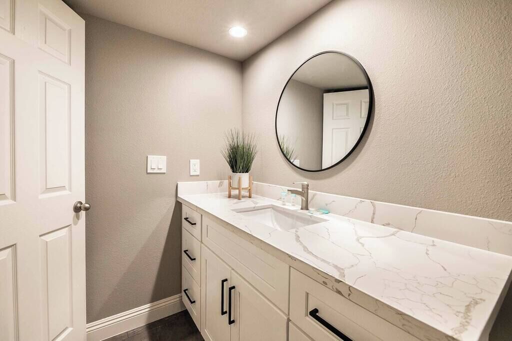 A bathroom with a white marble vanity, a round mirror, and a potted plant.