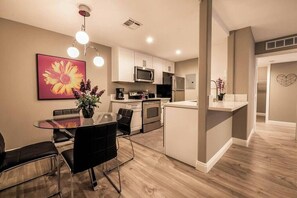 A modern kitchen with white cabinets, stainless steel appliances, and a dining area with a glass table and black chairs. - Carlton Suite 1b/1b near UNLV (Las Vegas)