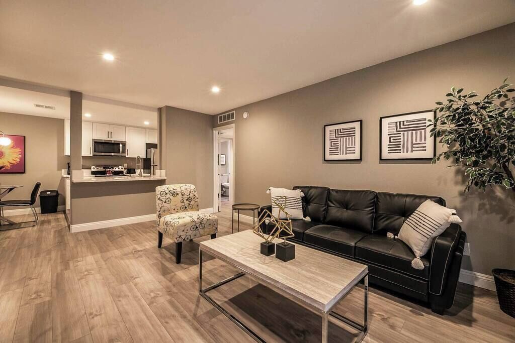 Ein modernes Wohnzimmer mit einer schwarzen Ledersofa, einem Couchtisch und einem Essbereich mit einem Stuhl und Tisch.