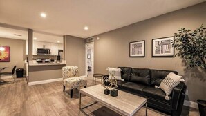 A modern living room with a black leather sofa, a coffee table, and a dining area with a chair and table. - Carlton Suite 1b/1b near UNLV (Las Vegas)