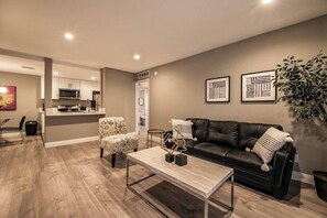 A modern living room with a black leather sofa, a coffee table, and a dining area with a chair and table. - Carlton Suite 1b/1b near UNLV (Las Vegas)