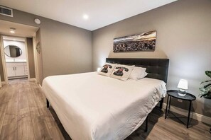 A modern bedroom with a large bed, a bedside table, a round mirror, and a cityscape painting on the wall. - Carlton Suite 1b/1b near UNLV (Las Vegas)