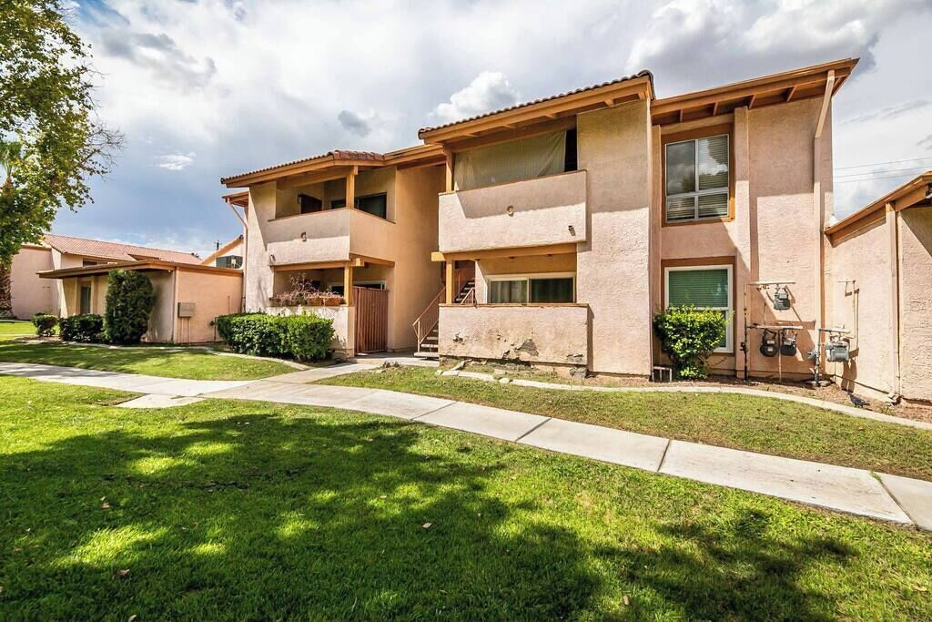 A multi-story residential building with balconies, a front entrance, and a well-maintained lawn.