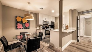 Una cocina moderna con armarios blancos, electrodomésticos de acero inoxidable y una mesa de comedor de vidrio con sillas negras.