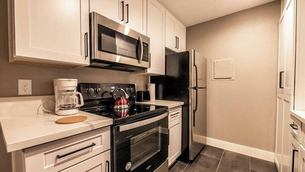 Una cocina moderna con electrodomésticos de acero inoxidable, armarios blancos y piso de baldosas.