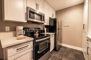 A modern kitchen with stainless steel appliances, white cabinetry, and a tiled floor. - Vermont Suite 1b/1b near UNLV (Las Vegas)