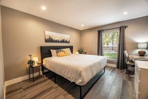 Quarto moderno com cama, mesa de cabeceira, abajur e vista para o exterior.