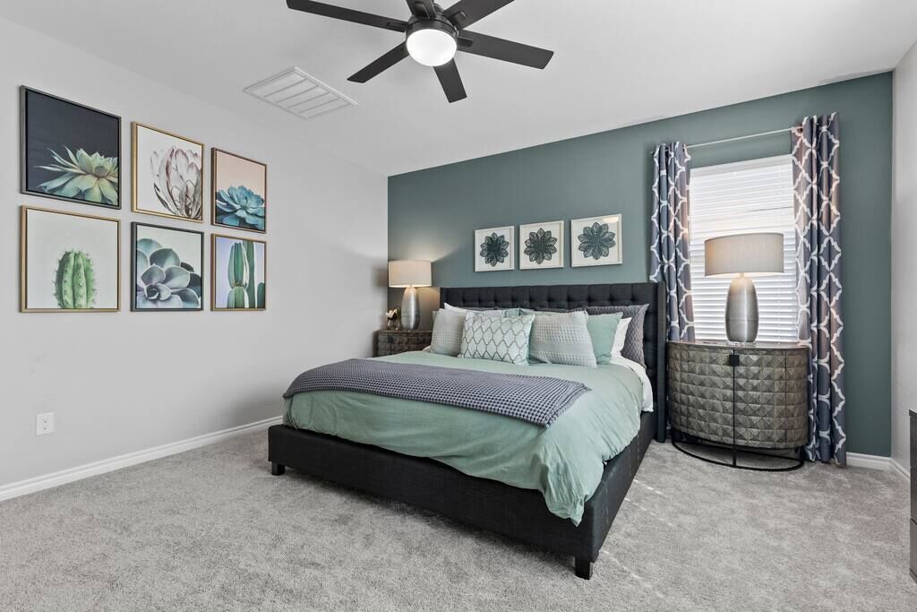 A bedroom with a bed, a ceiling fan, a nightstand, a lamp, and wall art.