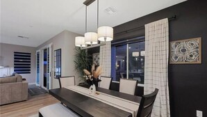 A modern dining area with a dark wood table, white chairs, and a hanging light fixture. - Skye Canyon 3 bedrooms + Loft (Las Vegas)