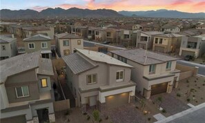 Un barrio residencial con casas modernas, cielo despejado y montañas a lo lejos.