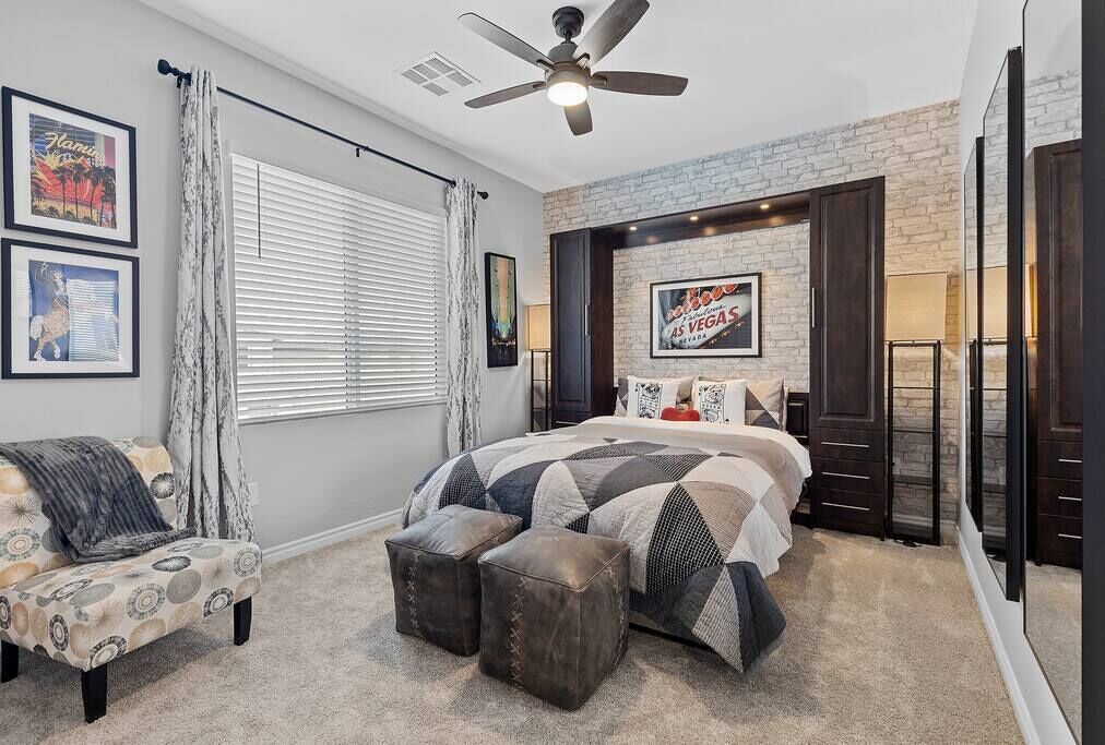 A bedroom with a bed, a chair, a ceiling fan, and a brick accent wall.