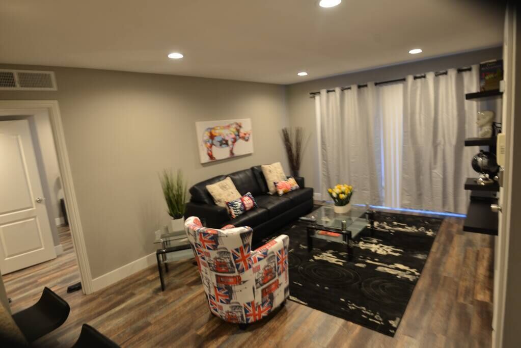A modern living room with a black sofa, a patterned armchair, a coffee table, and a decorative painting on the wall.