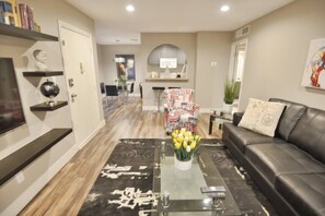 A modern living room with a glass coffee table, a black sofa, and a dining area in the background. - Crawford suite 1b/1b near UNLV (Las Vegas)