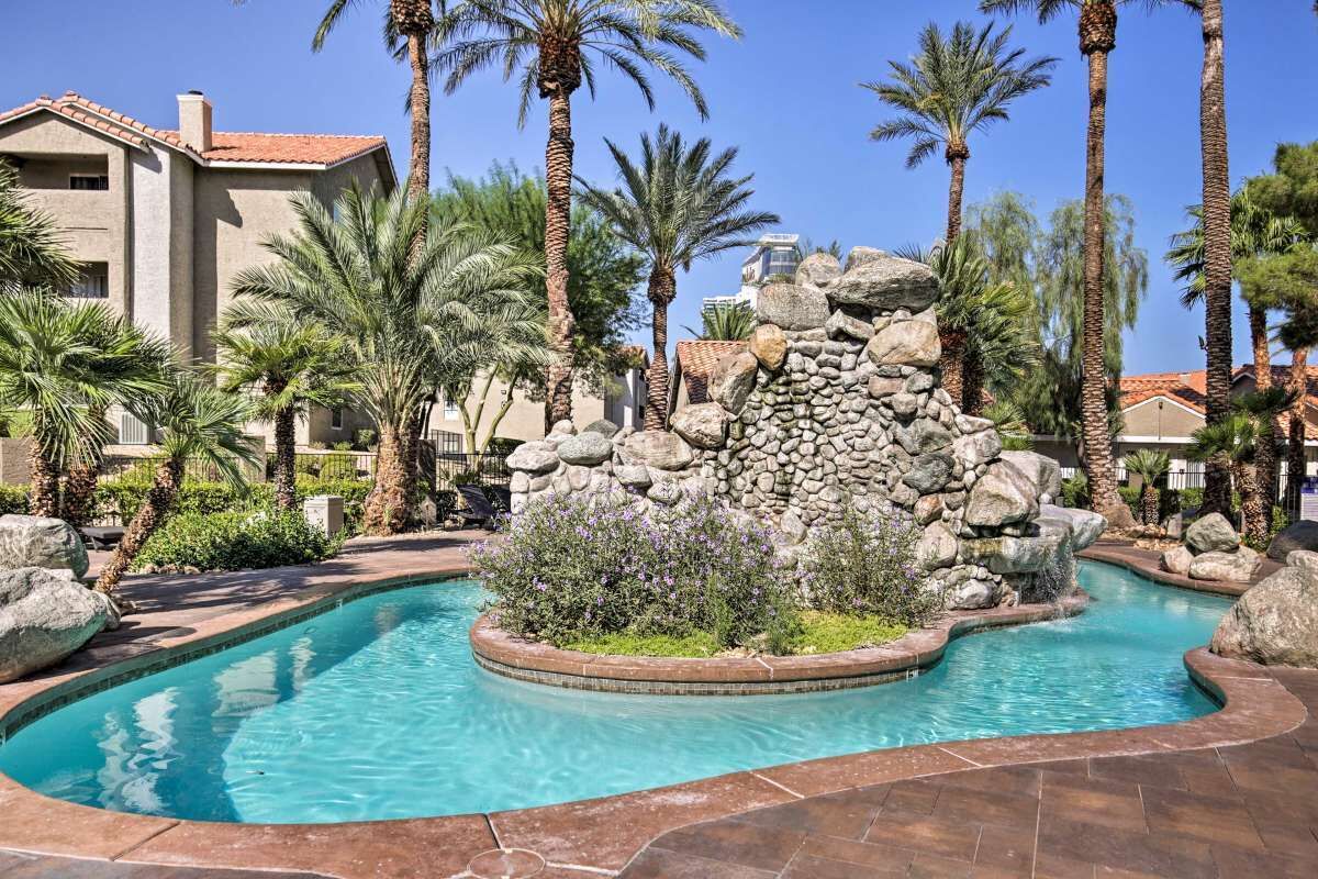 A swimming pool with a rock feature and palm trees.
