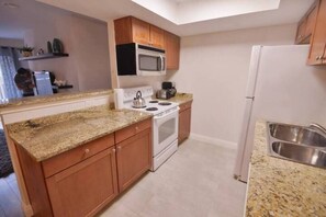 A compact kitchen with wooden cabinets, a microwave, a stove, and a sink. - Sunset Suite Great Condo 2bed/2bath near THE STRIP (Las Vegas)