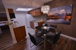 A modern kitchen with a dining area, featuring a glass table and chairs, wooden cabinets, and a large painting on the wall. - Sunset Suite Great Condo 2bed/2bath near THE STRIP (Las Vegas)