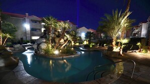 Ein Poolbereich bei Nacht mit einer Steinsäule, Palmen und Liegestühlen.