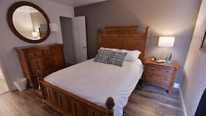 A bedroom with a wooden bed, a dresser, a nightstand, a mirror, and a door.