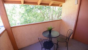A small balcony with a round table and two chairs, a potted plant, and a view of trees through a window. - Nova Suite 1b/1b close to strip! (Las Vegas)