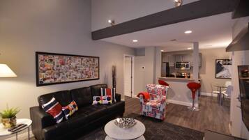A modern living room with a black leather sofa, a round coffee table, and a colorful abstract painting on the wall.