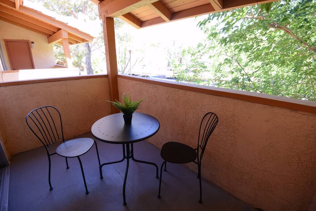 Eine überdachte Terrasse mit einem runden Tisch, zwei Stühlen, einem Blumentopf und Blick auf Bäume.