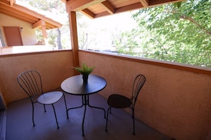 A covered patio with a round table and two chairs, a potted plant, and a view of trees. - Nova Suite 1b/1b close to strip! (Las Vegas)
