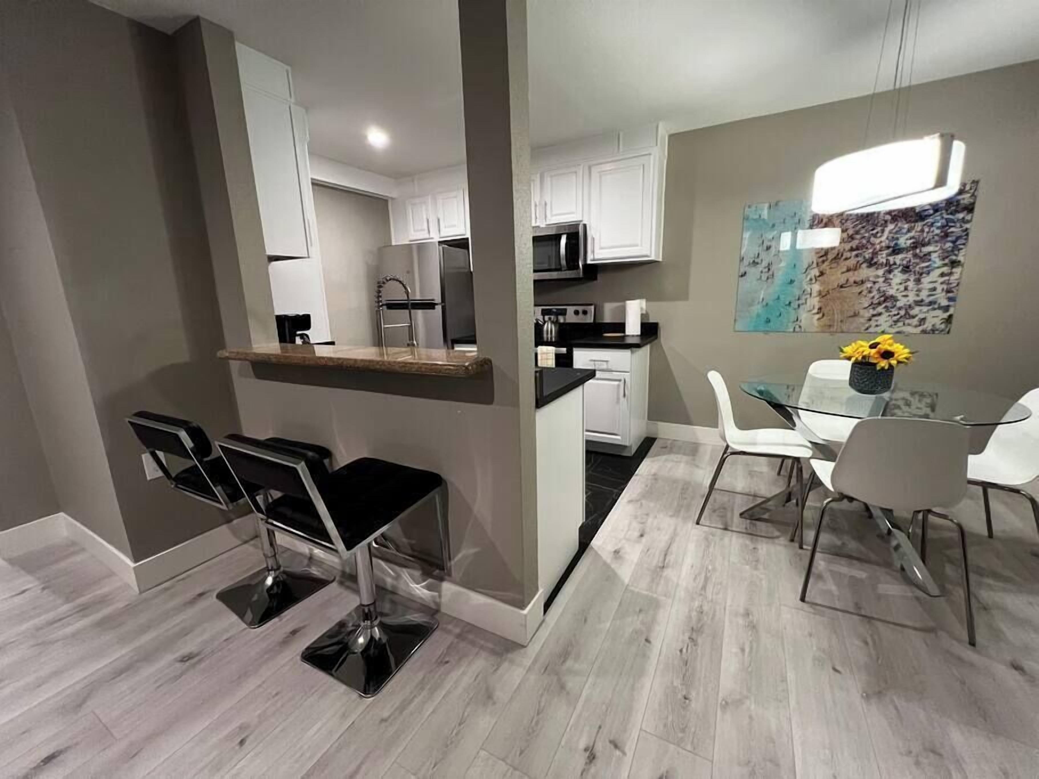 A modern kitchen with white cabinets, a microwave, and a dining area with a glass table and chairs.