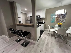 A modern kitchen with white cabinets, a microwave, and a dining area with a glass table and chairs. - Onyx suite 2b/1b Near Strip (Las Vegas)