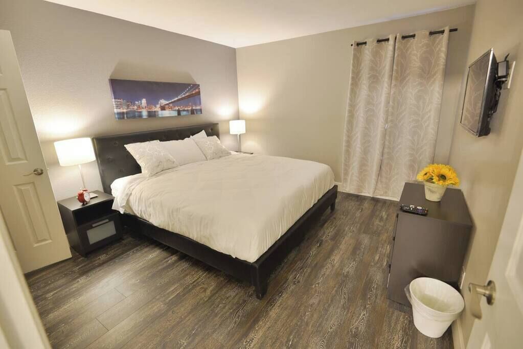 Een hotelkamer met een bed, nachtkastjes, een lamp, een schilderij aan de muur, een gordijn en een tafeltje met een vaas.
