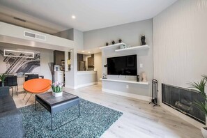 A modern living room with a flat-screen TV, a fireplace, and a staircase leading to another level. - Ruxley Suite Luxury 2b/2b condo (Las Vegas)