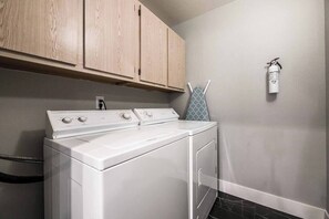 A laundry area with a front-loading washer and dryer, wooden cabinets above, and a wall-mounted fire extinguisher. - Ruxley Suite Luxury 2b/2b condo (Las Vegas)
