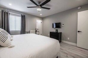 Ein Schlafzimmer mit einem Bett, einem Deckenventilator, einem Fernseher auf einem Schrank und einer Tür.