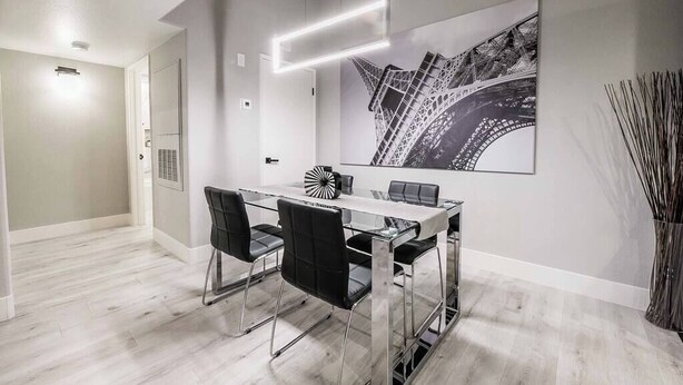 A modern dining area with a glass table, black chairs, and a large black-and-white artwork of a bridge. - Ruxley Suite Luxury 2b/2b condo (Las Vegas)