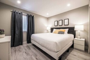 A bedroom with a bed, bedside tables, a nightstand, a window with curtains, and wall-mounted pictures. - Ruxley Suite Luxury 2b/2b condo (Las Vegas)