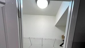 Un pasillo estrecho con una puerta blanca a la izquierda, una pared blanca y un suelo de madera gris.