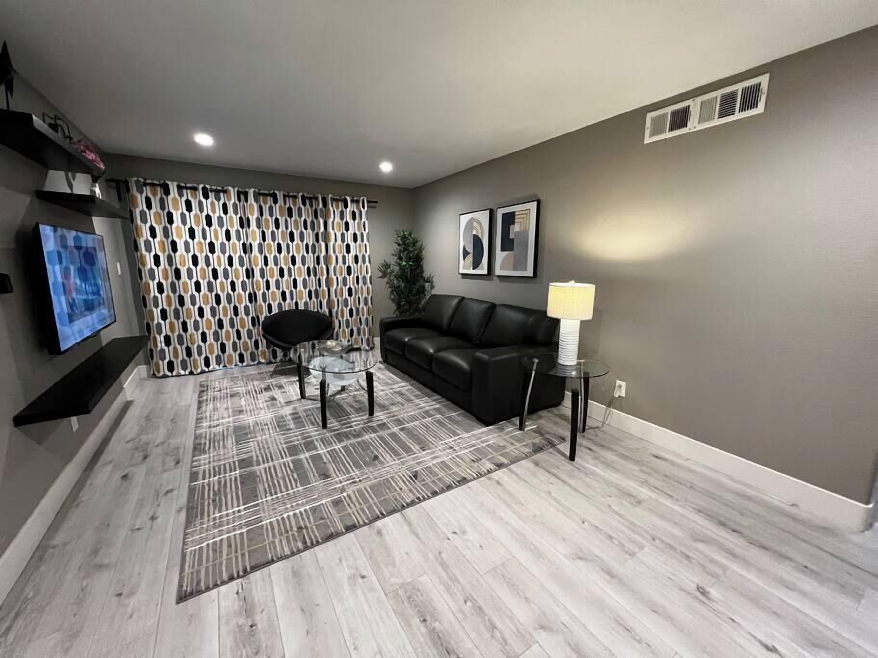 A living room with a black leather sofa, a glass coffee table, and a patterned rug.