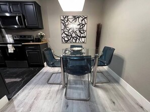 A compact kitchen with a dining area, featuring a glass table and chairs, a microwave, and a coffee maker. - Laguna Suite 2b/1b Near Strip (Las Vegas)