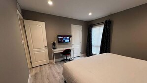 Un dormitorio con cama, escritorio, silla, televisor y ventana con cortinas.