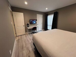 Ein Schlafzimmer mit einem Bett, einem Schreibtisch, einem Stuhl, einem Fernseher und einem Fenster mit Vorhängen.