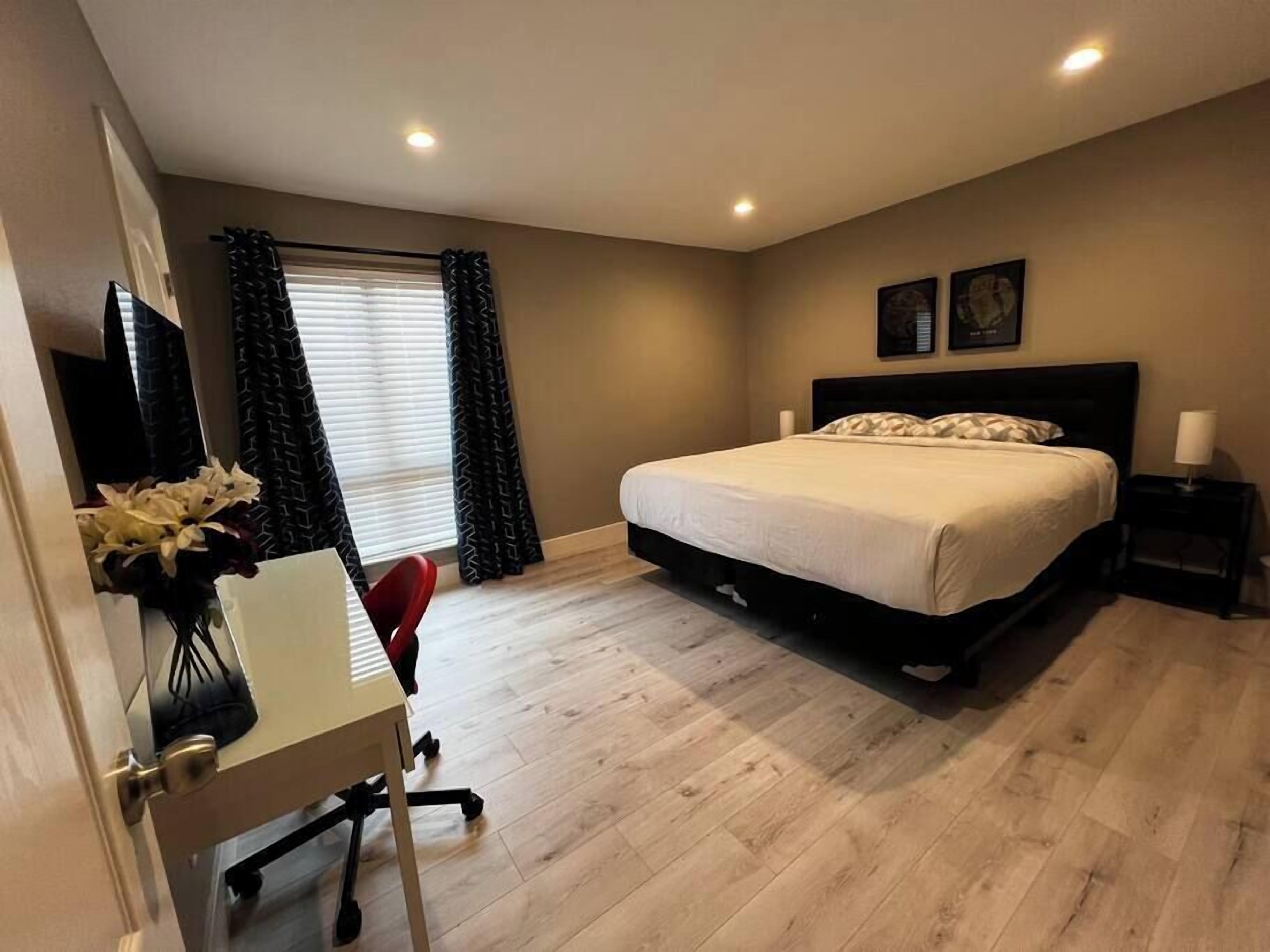 Une chambre à coucher comprenant un lit, un bureau, une chaise, une fenêtre avec des rideaux et une œuvre d’art accrochée au mur.