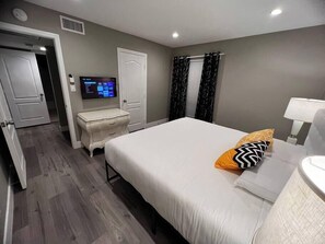 Ein Hotelzimmer mit Bett, Nachttisch, Lampe und Fernseher an der Wand.
