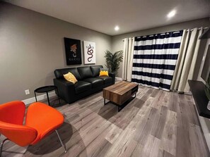 Ett modernt vardagsrum med en svart lädersoffa, ett träbord och en randig gardin.
